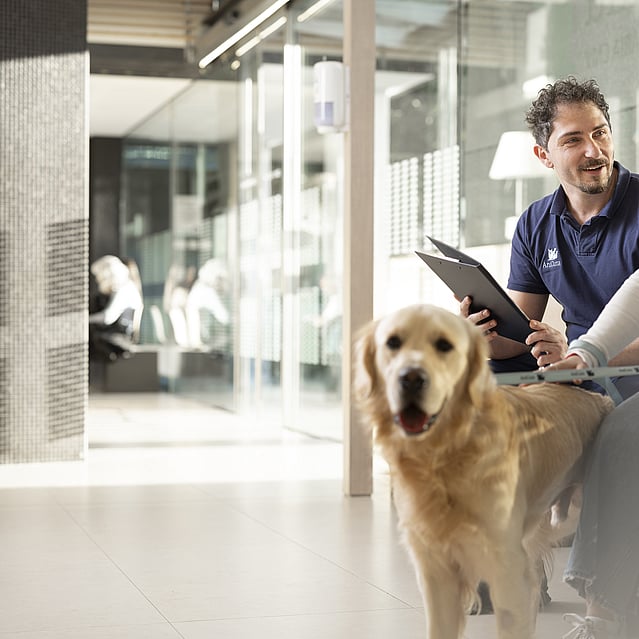 Kvinnlig hundägare pratar med en AniCura-anställd. Framför dem sitter en hund.