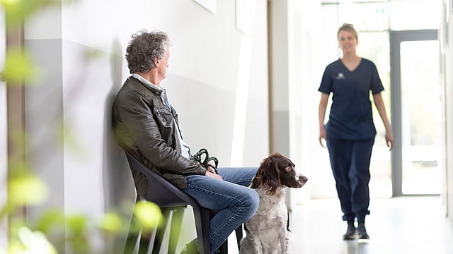 En man sitter med sin hund och väntar på veterinären.