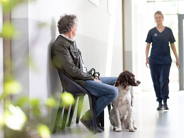 En man sitter med sin hund och väntar på veterinären.