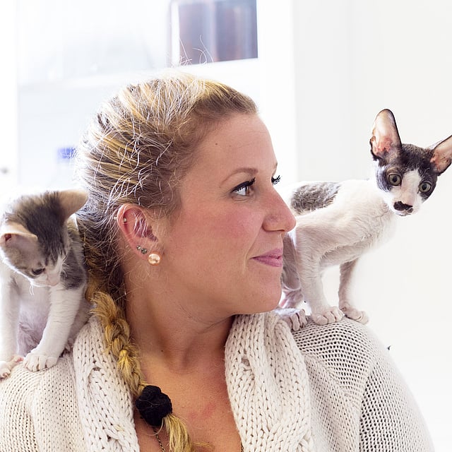 Två svartvita katter sitter på en blond kvinnas axlar.