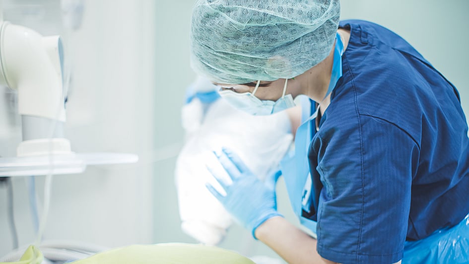 Veterinär iklädd blåa vårdkläder och skyddsmask tar hand om sjukt djur.