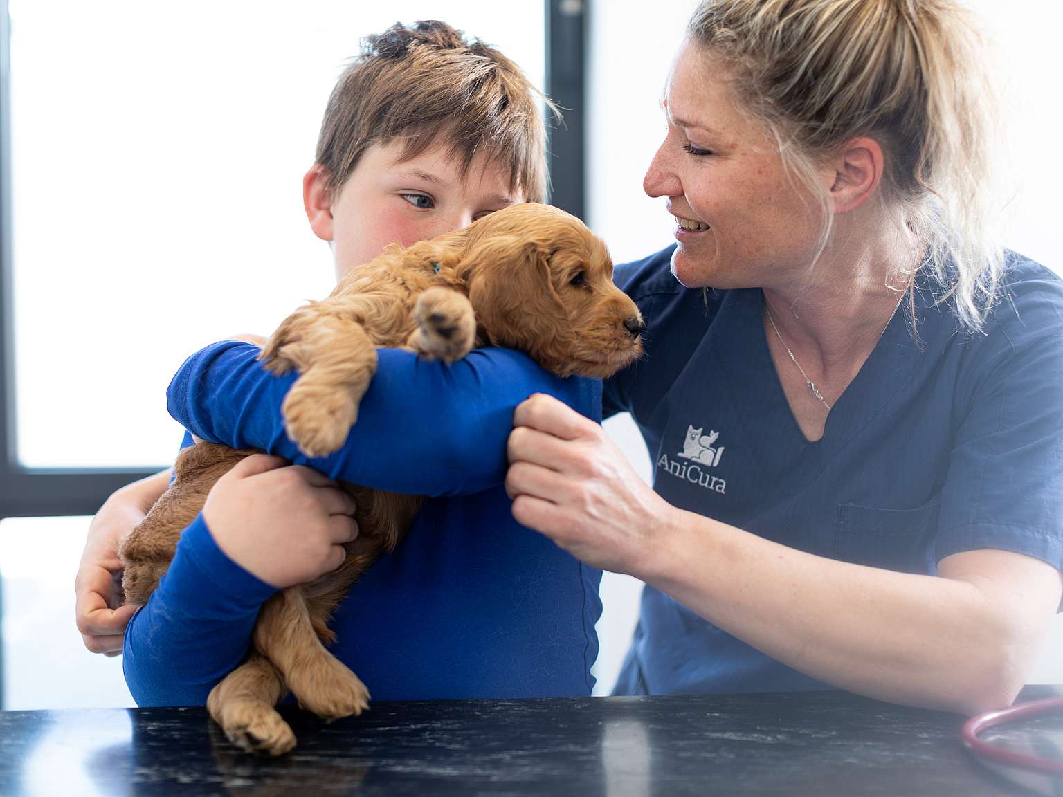A boy is holding a puppy and a veterinatian stands beside them.
